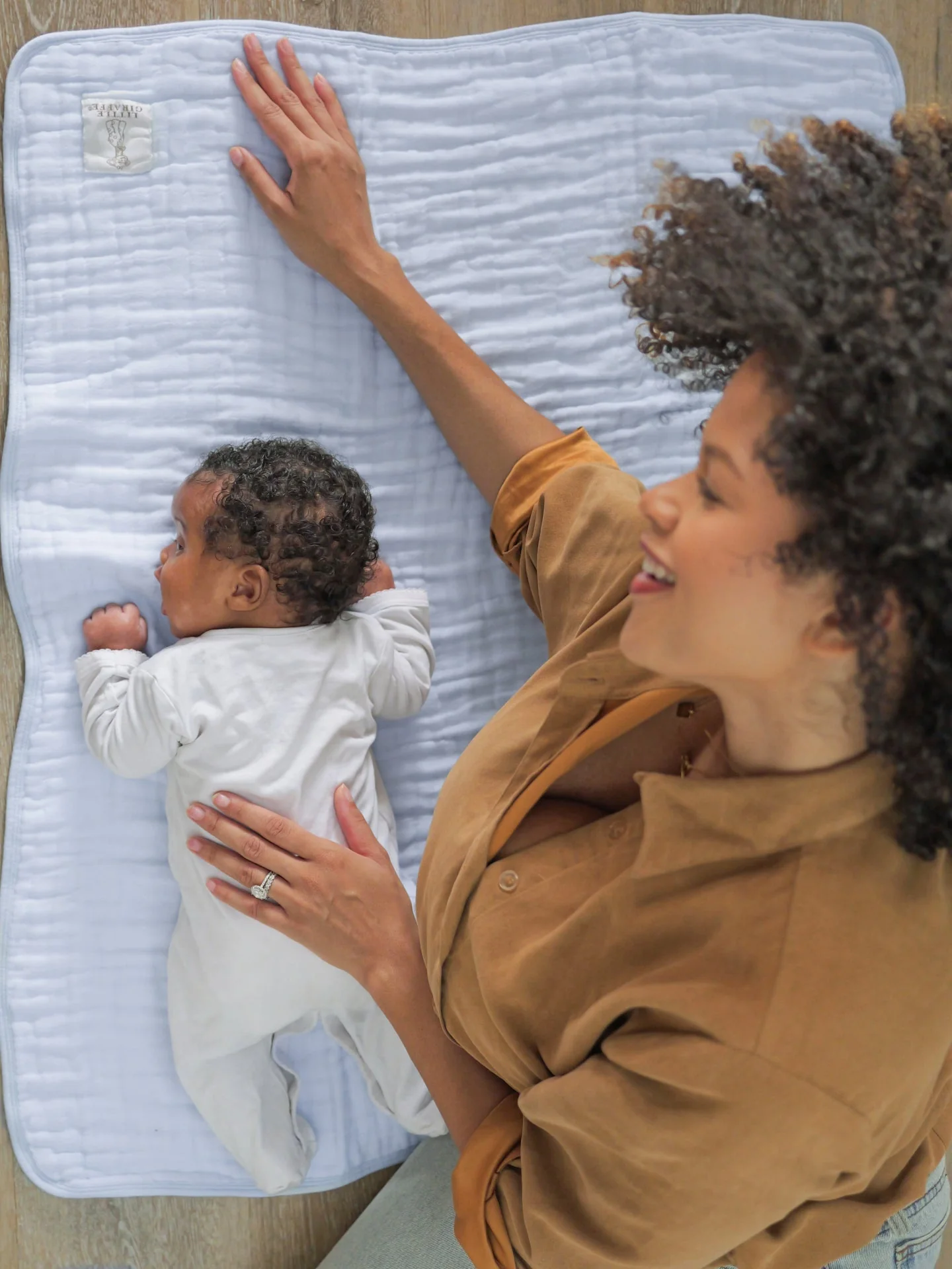 Adult holding an awake baby beside a blue Little Giraffe cotton blanket